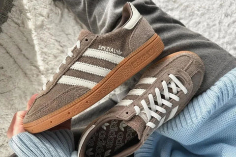 Adidas handball spezial Casually placed on the legs of a person wearing grey trousers and a blue knitted sweater, with a light grey plush carpet in the background, showing the casual lifestyle attitude of Adidas handball spezial